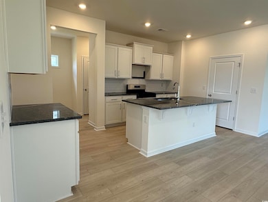 Kitchen with light wood-type flooring, white cabinets, gas range, a breakfast bar, and recessed lighting