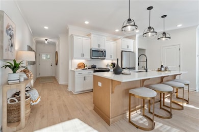 Kitchen with stainless steel appliances, a sink, a center island with sink, baseboards, and ornamental molding