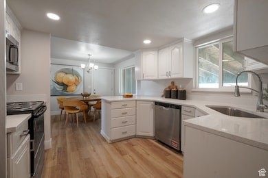 Kitchen featuring a chandelier, appliances with stainless steel finishes, light wood finished floors, white cabinets, and decorative light fixtures