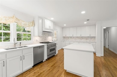 Kitchen featuring appliances with stainless steel finishes, a sink, decorative backsplash, white cabinets, and light wood-type flooring