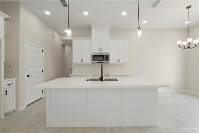 Kitchen with stainless steel microwave, a sink, white cabinetry, a kitchen island with sink, and light wood-style floors