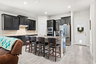 Kitchen with backsplash, appliances with stainless steel finishes, a breakfast bar area, light stone counters, and a center island with sink