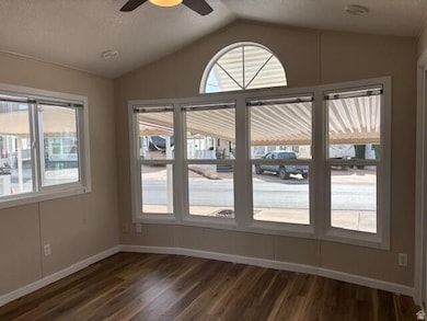 Unfurnished dining area featuring a textured ceiling, vaulted ceiling, dark wood-style floors, and a ceiling fan
