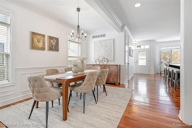 Dining room with crown molding, light wood finished floors, a chandelier, wainscoting, and recessed lighting