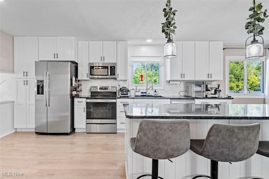 Kitchen featuring appliances with stainless steel finishes, a breakfast bar area, light wood-type flooring, white cabinetry, and pendant lighting