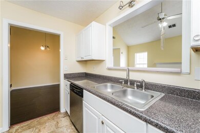 Kitchen featuring dishwasher, a sink, dark countertops, vaulted ceiling, and white cabinetry