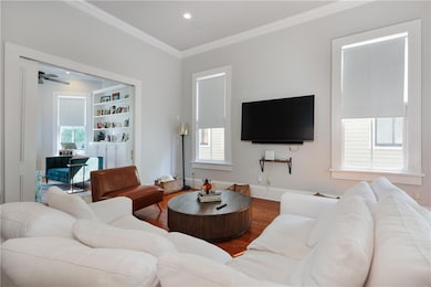 Living room with wood finished floors, ornamental molding, a ceiling fan, pocket doors, and recessed lighting