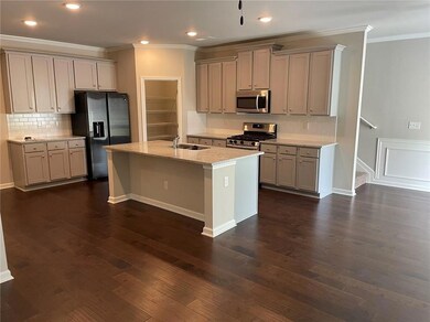 Kitchen featuring dark wood-type flooring, stainless steel appliances, an island with sink, backsplash, and sink
