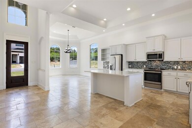 Kitchen with a raised ceiling, a kitchen island, decorative light fixtures, stainless steel appliances, and white cabinetry