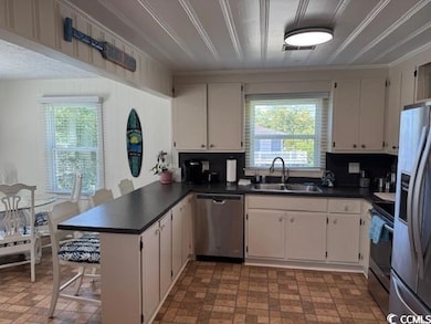 Kitchen featuring a peninsula, stainless steel appliances, dark countertops, brick patterned floors, and crown molding