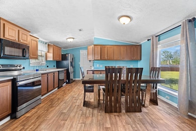 Kitchen with black appliances, light wood-style floors, light countertops, lofted ceiling, and a textured ceiling