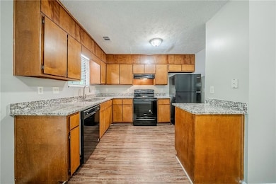 Kitchen with black appliances, a sink, under cabinet range hood, brown cabinets, and light wood-type flooring