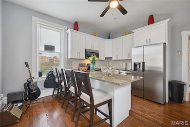 Kitchen featuring stainless steel appliances, light stone countertops, a kitchen bar, white cabinetry, and a peninsula