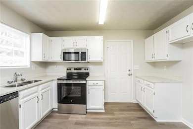 Kitchen featuring stainless steel appliances, white cabinets, light wood-type flooring, light countertops, and a textured ceiling