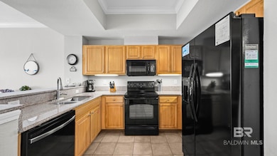Kitchen featuring crown molding, black appliances, light stone counters, light tile patterned floors, and a tray ceiling