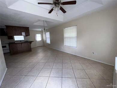 Unfurnished living room featuring light tile patterned floors, ceiling fan, a tray ceiling, a chandelier, and baseboards