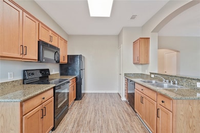Kitchen with black appliances, light wood-type flooring, arched walkways, and light stone countertops