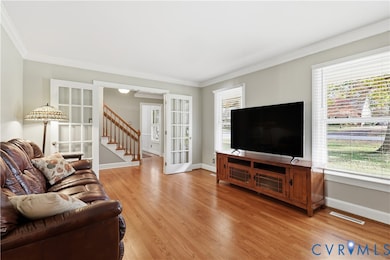 Living room featuring crown molding, light hardwood floors, and French door entry from the front foyer.