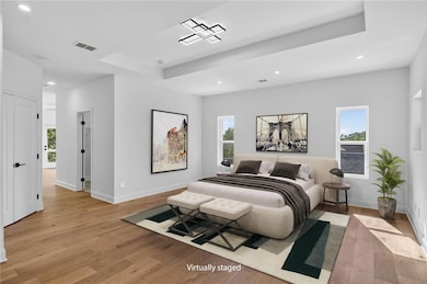 Bedroom featuring light wood-type flooring, a raised ceiling, recessed lighting, and multiple windows