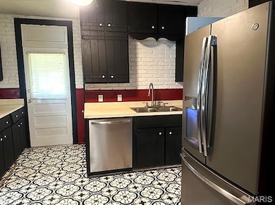 Kitchen with appliances with stainless steel finishes, brick wall, light countertops, and dark cabinets