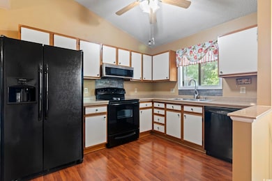 Kitchen with black appliances, a sink, lofted ceiling, white cabinets, and dark wood-style flooring