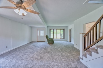 Unfurnished living room featuring a textured ceiling, carpet, stairs, baseboards, and ceiling fan