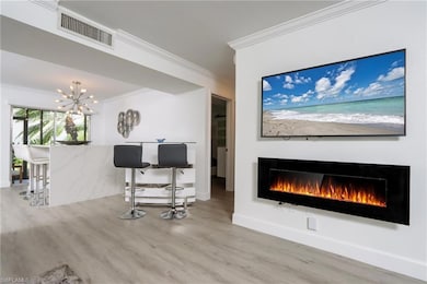 Living room featuring ornamental molding, a warm lit fireplace, wood finished floors, and a chandelier