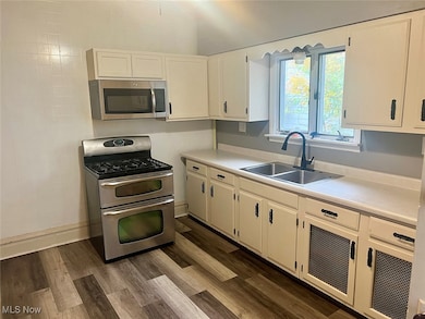 Kitchen featuring appliances with stainless steel finishes, light countertops, dark wood-type flooring, and white cabinetry