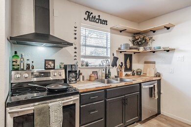 Kitchen with appliances with stainless steel finishes, butcher block countertops, wall chimney exhaust hood, light wood-type flooring, and open shelves