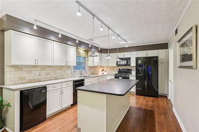Kitchen with black appliances, light wood-type flooring, white cabinets, tasteful backsplash, and a textured ceiling