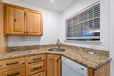 Kitchen with light stone counters, white dishwasher, and a textured wall