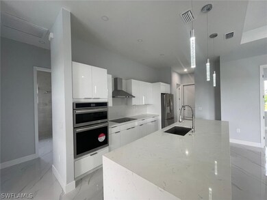 Kitchen featuring decorative light fixtures, wall chimney range hood, stainless steel appliances, white cabinets, and sink