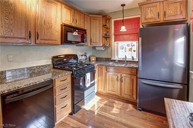 Kitchen with black appliances, hanging light fixtures, light wood-type flooring, and sink