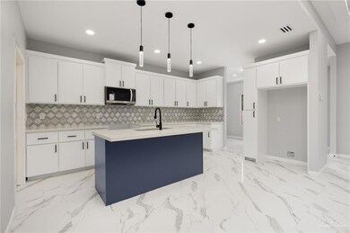 Kitchen with white cabinets, decorative light fixtures, a center island with sink, and sink