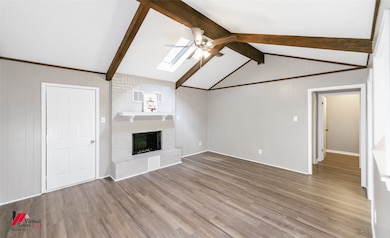 Unfurnished living room with a skylight, wood finished floors, a brick fireplace, wooden walls, and a ceiling fan