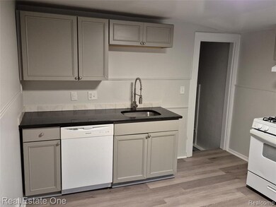 Kitchen with gray cabinetry, white appliances, and light wood-style flooring