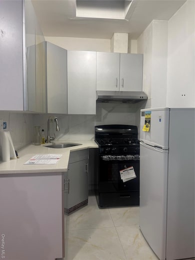 Kitchen featuring refrigerator, gray cabinets, range, tasteful backsplash, and ventilation hood