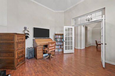 Home office featuring french doors, crown molding, Pergo Premium flooring, a high ceiling, and a notable chandelier