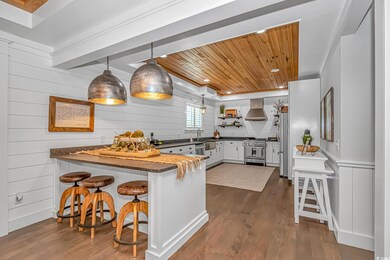 Kitchen with wooden ceiling, a peninsula, appliances with stainless steel finishes, dark wood-style floors, and ventilation hood