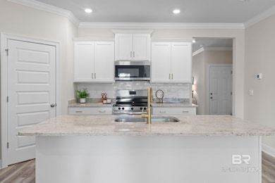 Kitchen with white cabinetry, light wood-style flooring, backsplash, crown molding, and light stone countertops