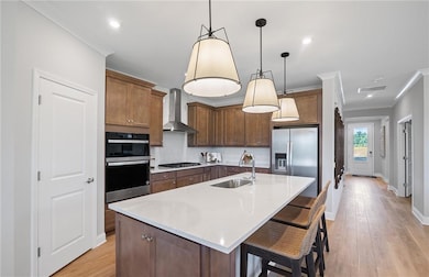 Kitchen with a sink, wall chimney range hood, stainless steel appliances, ornamental molding, and decorative backsplash