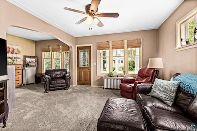 Carpeted living room with arched walkways, a ceiling fan, and radiator heating unit