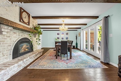 Dining room with a chandelier, baseboards, a brick fireplace, hardwood / wood-style flooring, and beam ceiling