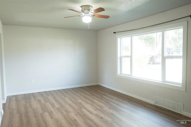 Empty room with light wood-style floors, ceiling fan, and a textured ceiling