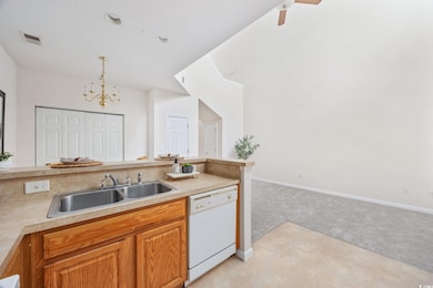 Kitchen featuring dishwasher, light colored carpet, pendant lighting, light countertops, and a chandelier