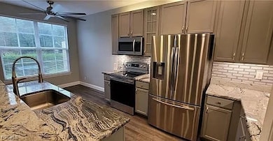 Kitchen featuring light stone counters, backsplash, stainless steel appliances, and dark wood finished floors