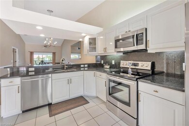 Kitchen with stainless steel appliances, a peninsula, a chandelier, white cabinets, and lofted ceiling