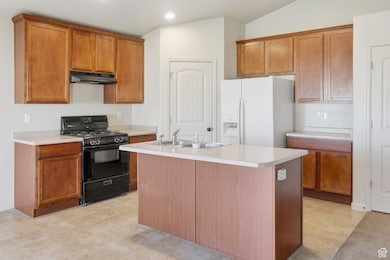 Kitchen featuring black range with gas stovetop, white refrigerator with ice dispenser, light countertops, brown cabinets, and recessed lighting