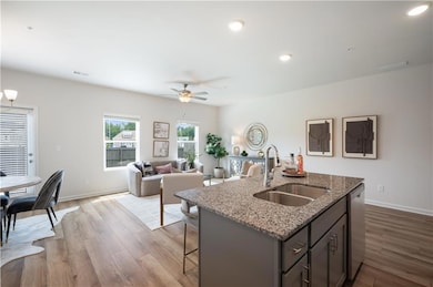 Kitchen with light stone counters, light wood-style flooring, an island with sink, ceiling fan, and recessed lighting