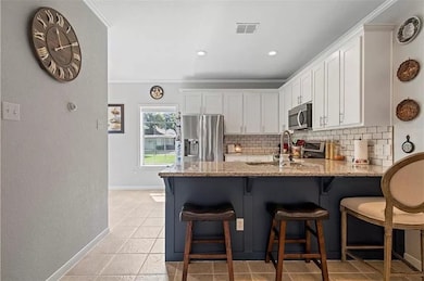 Kitchen with white cabinets, a kitchen breakfast bar, appliances with stainless steel finishes, tasteful backsplash, and light stone countertops